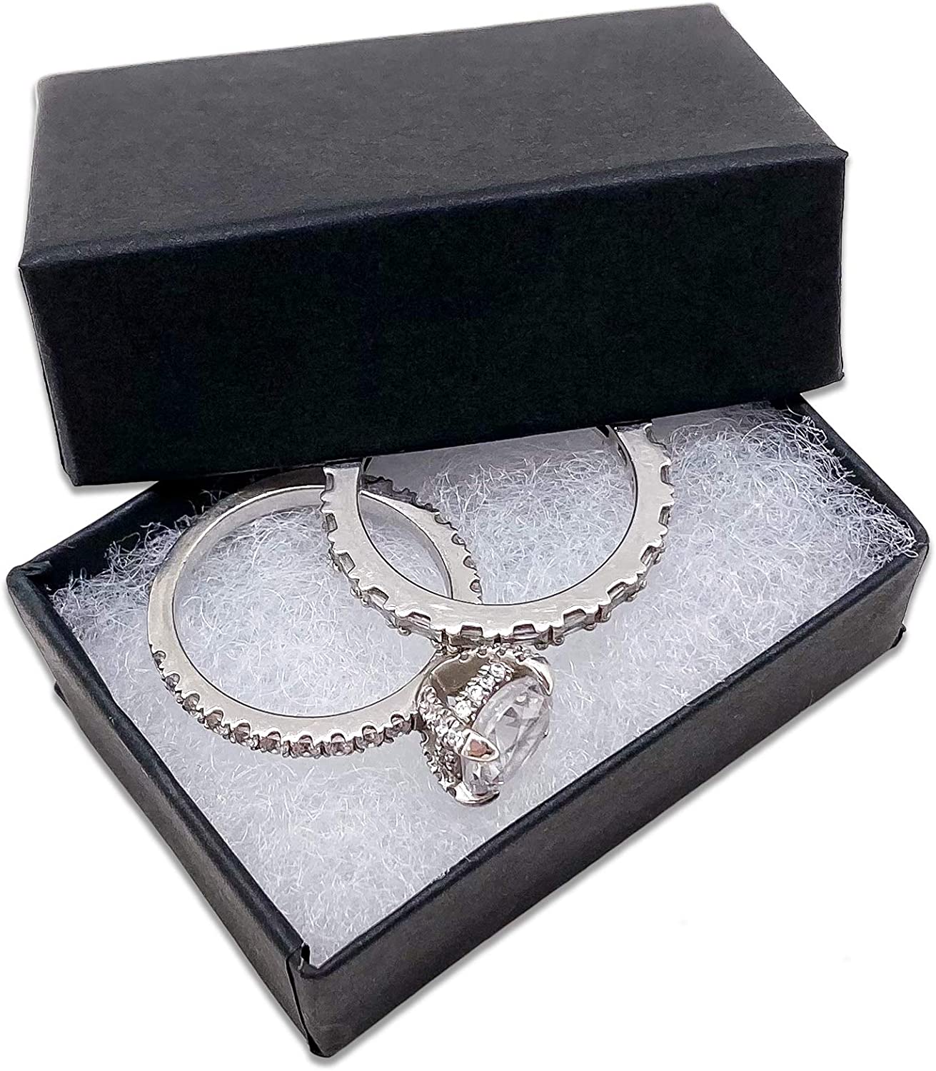 A black cardboard jewelry box with the lid opened revealing cotton filling with two silver rings inside the box.